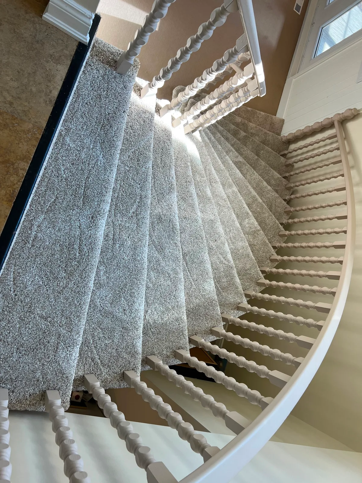 Looking down a curved flight carpeted in silver grey, the treads narrowing into winders as the stair turns past white bobbin spindles