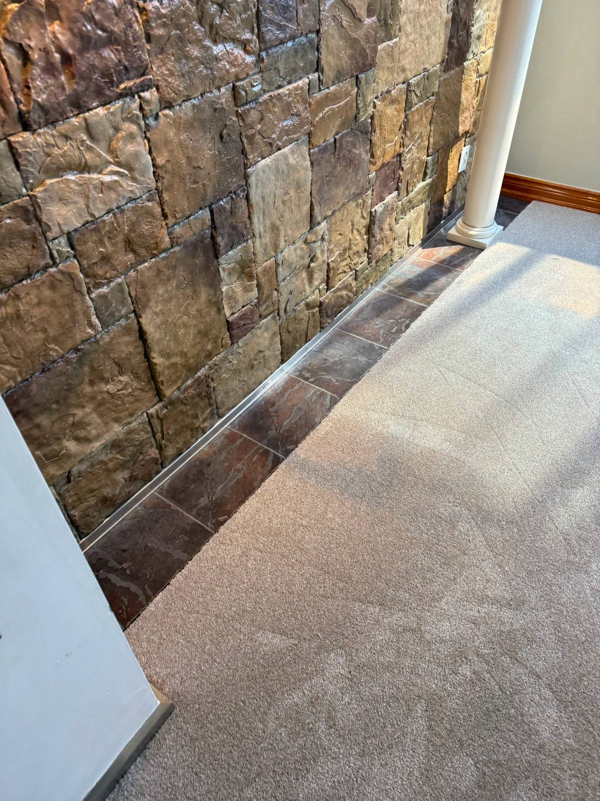 The same carpet running up to a slate tile border along a stone feature wall, finished with a metal edge strip
