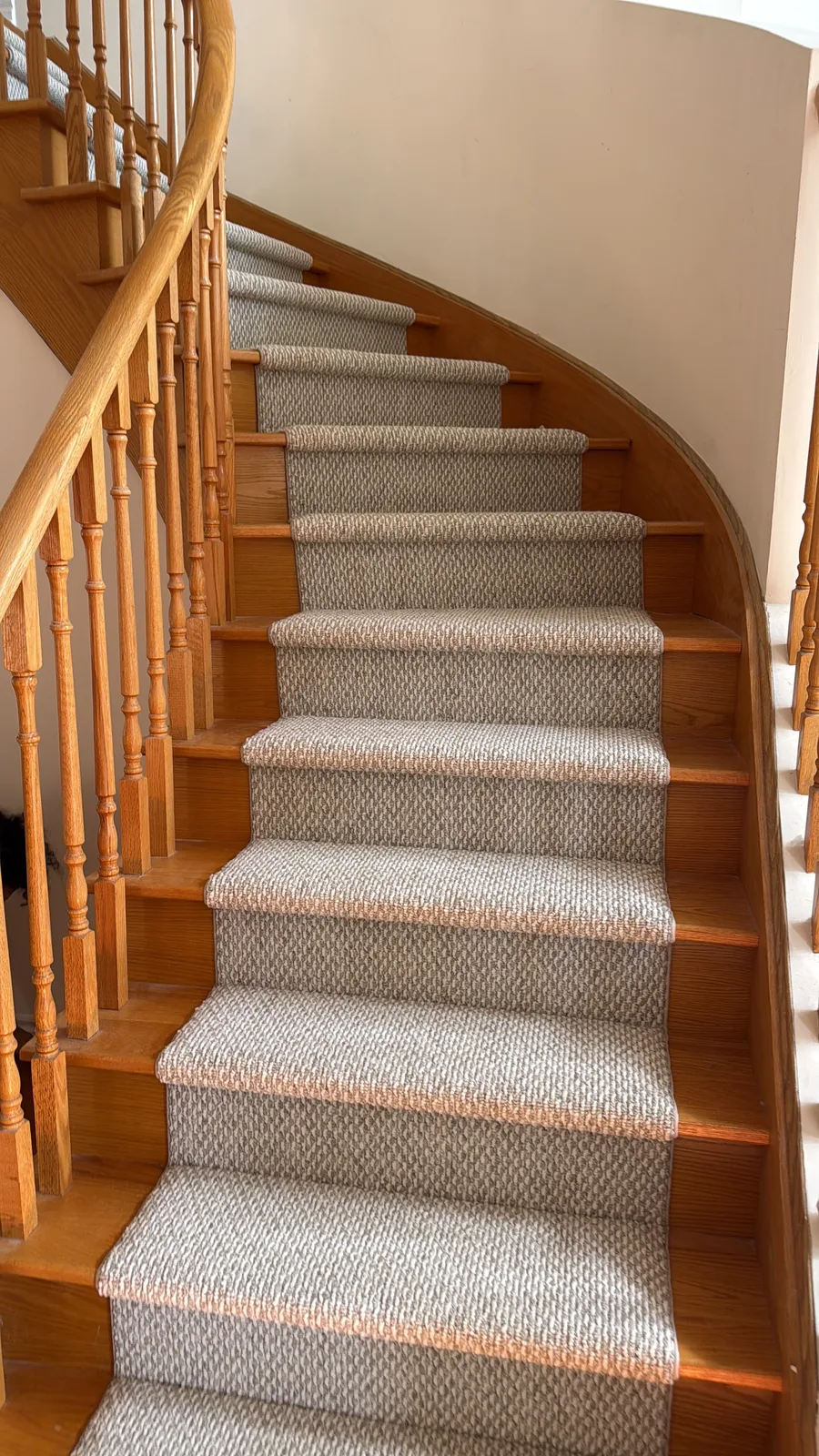 A bound centre runner on a curved oak staircase, held to an even margin of bare oak on both sides as the flight turns