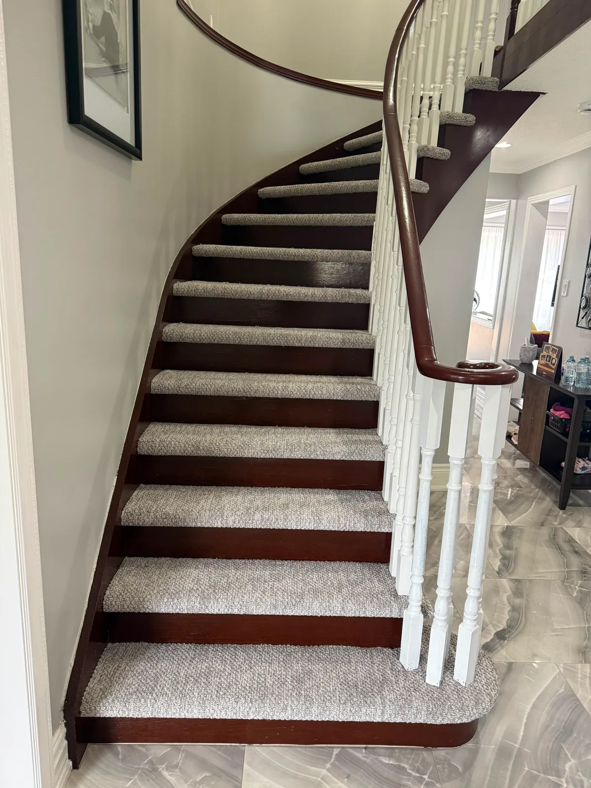 A curved staircase with carpet inset on each tread, wrapped around the rounded bottom step, with the dark stained risers left bare