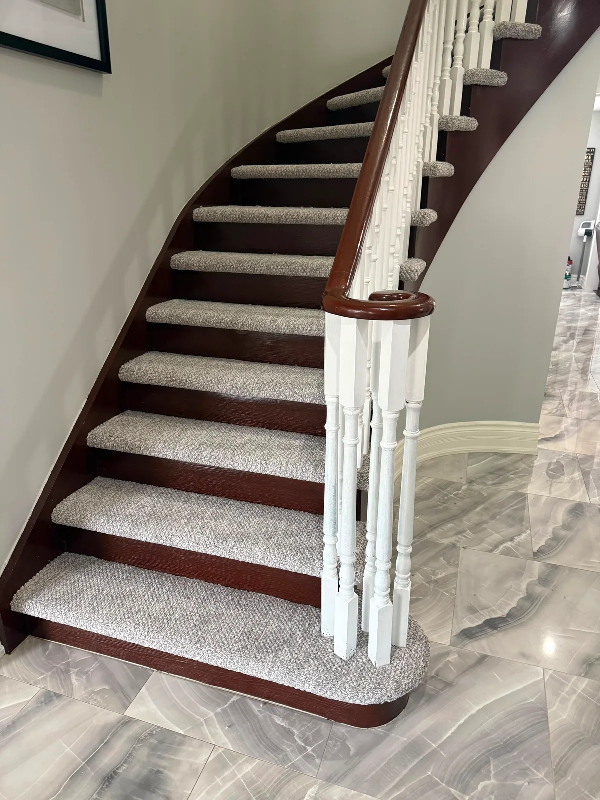 The bottom of the curved staircase, where the carpet wraps the rounded starting step against the marble floor