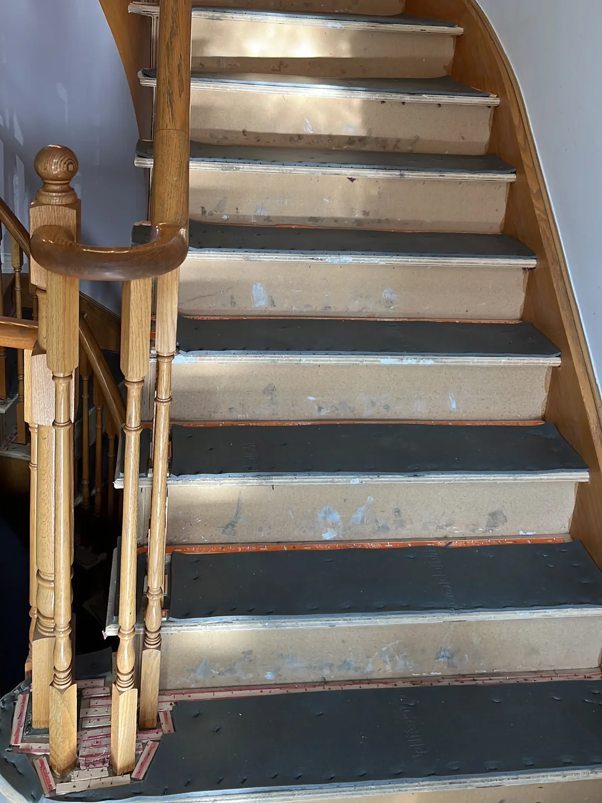 A curved staircase stripped back to bare treads, with gripper rods fitted and the old adhesive still showing