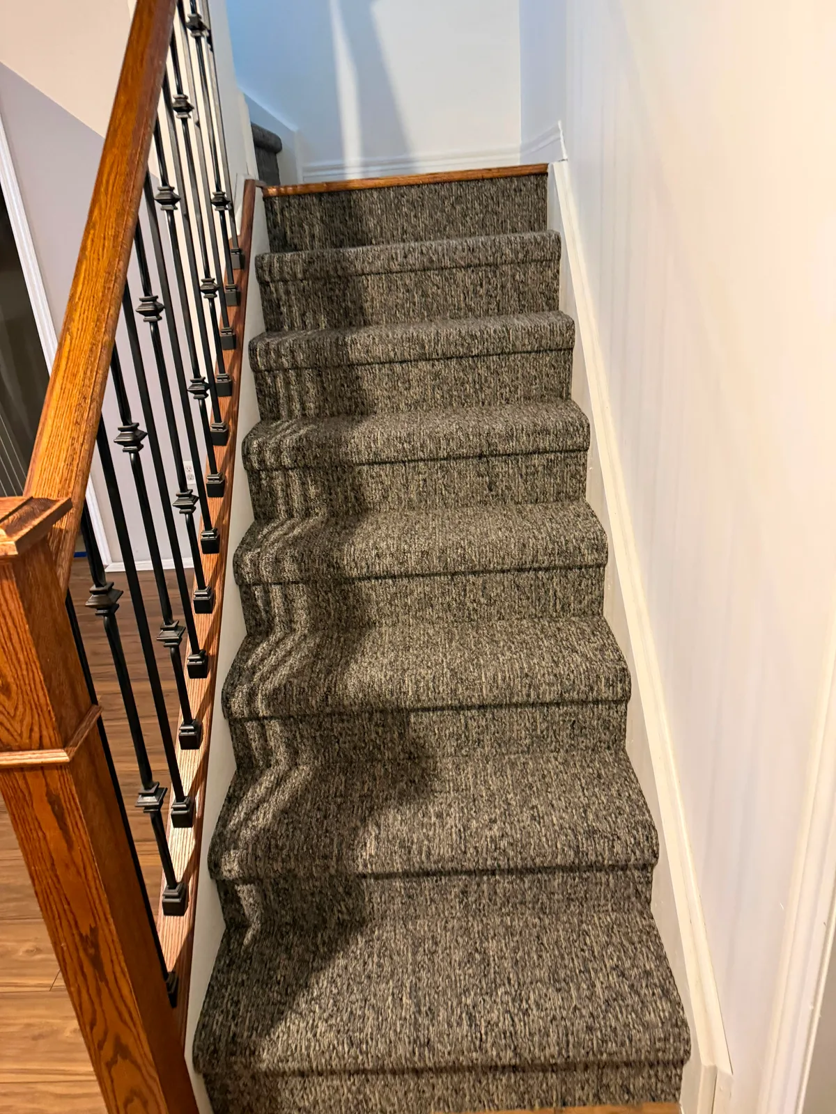 A straight flight carpeted in a dark heathered tweed, run between an oak rail with black iron balusters and a plain white wall