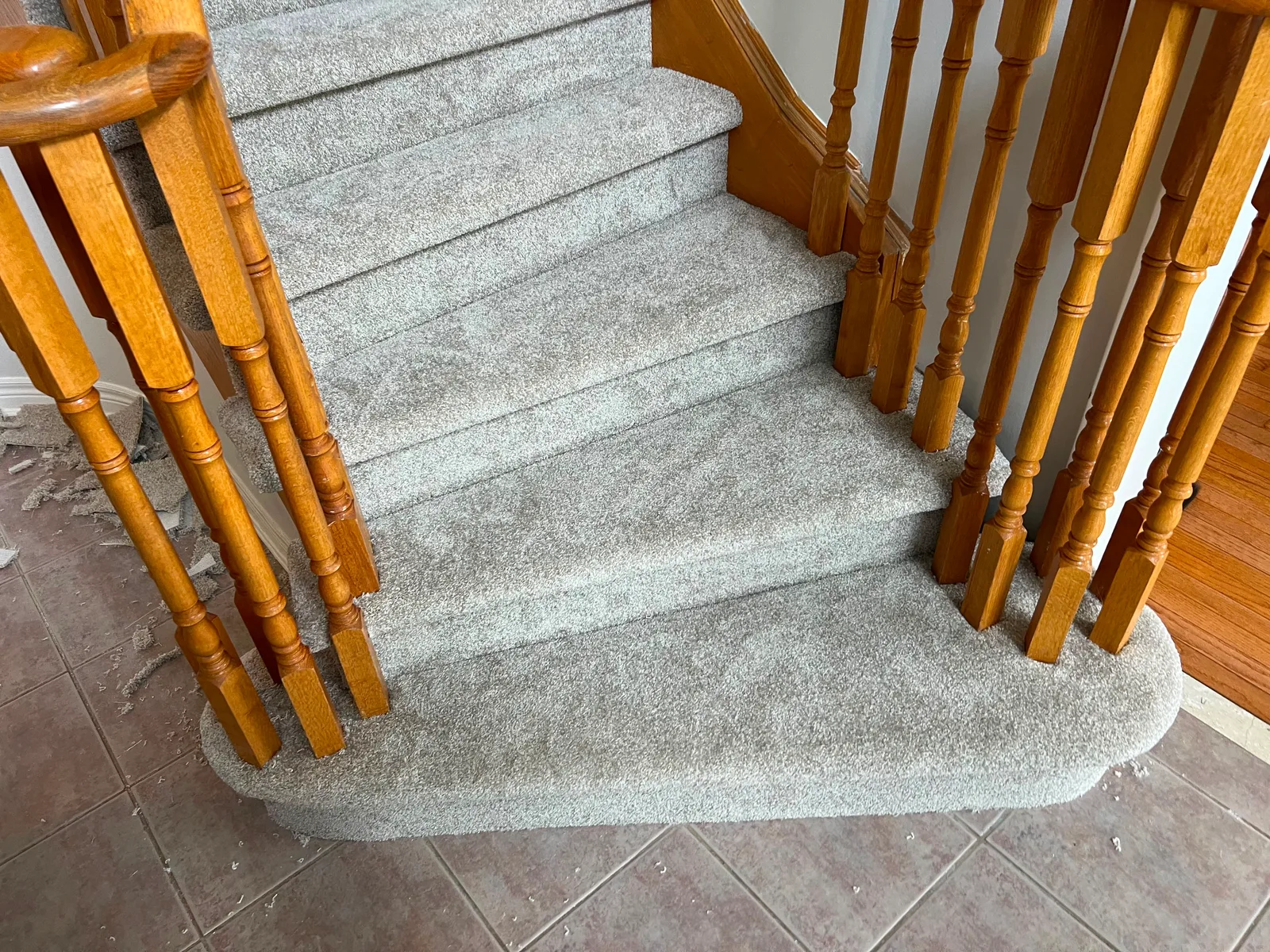 A rounded starting step wrapped in carpet, finished tight around the oak spindles and down to the tile